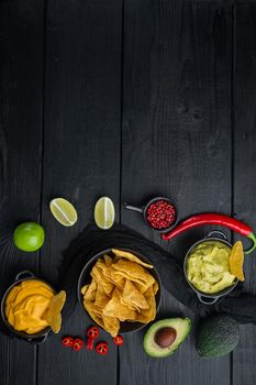 Mexican crispy snack, nachos chips and cheese guacamole avocado sauces, on black wooden background, top view or flat lay with copy space for text