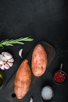 Sweet potato or batat with herbs and spices on black background, top view with space for text.