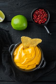 Bowl with cheese dip with nacho, on black wooden background, top view or flat lay