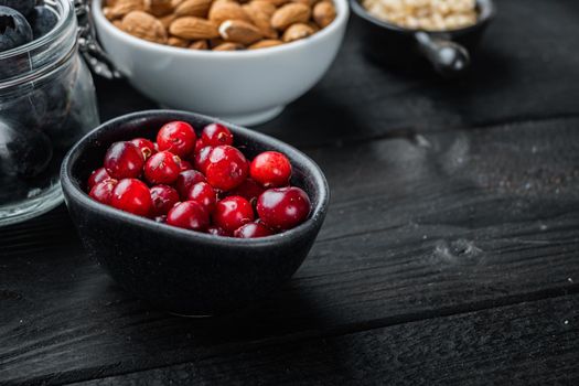 Cranberry, ripe red berry in bowl with space for text, on black wooden background.