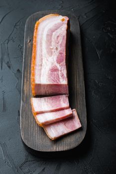 Smoked bacon, whole slab on black background.