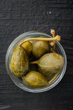 Capers, marinated in oil, on black wooden background, flat lay