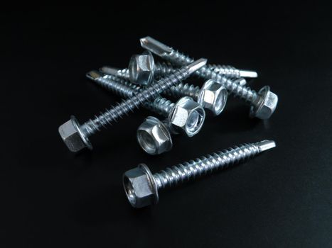 small amount Self-tapping screws galvanized with a semicircular head and a hex head on a black background.