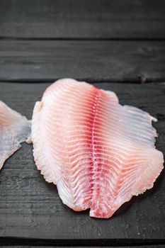 Raw tilapia fish fillet meat cuts, on black wooden background