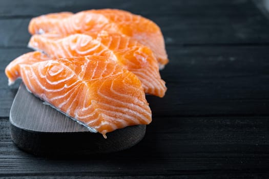Portion set of salmon fillet, on black wooden table with space for text