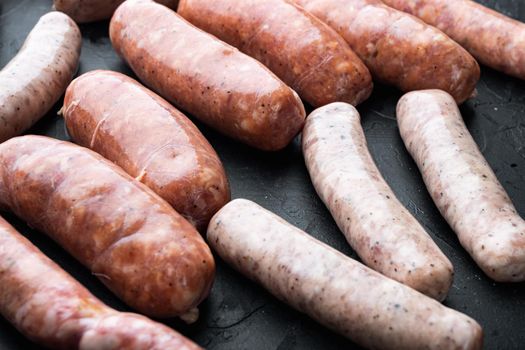 Fresh raw pork, beef and chicken sausages, on black background.