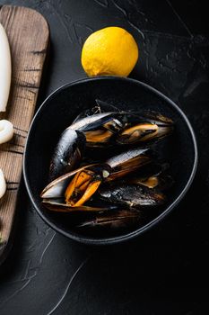 Steamed mussels in black bowl on black concrete surface, flat lay, food photo.