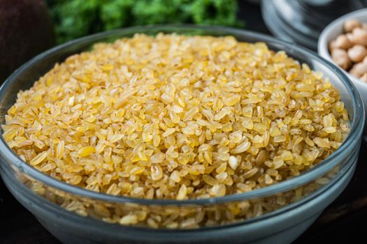 Bulgur grain in bowl on dark wooden background.