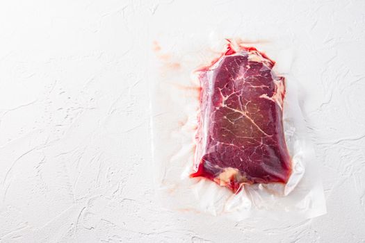 Vacuum packed organic beef meat rump steak on white concrete textured background, top view space for text