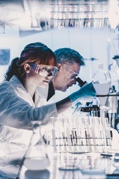 Health care researchers working in life science laboratory. Young female research scientist and senior male supervisor preparing and analyzing microscope slides in research lab.