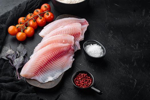 Raw white fish tilapia, with basmati rice and cherry tomatoes ingredients, on black background