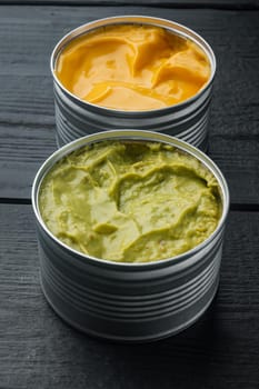 Canned cheese and guacamole sauce in can, on black wooden background