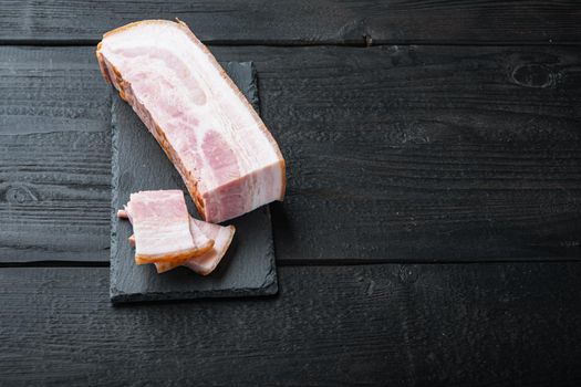 Bacon pancetta cut and sliced on black wooden table with space for text.