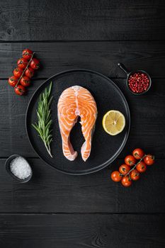 Slice of red fish trout with herbs, on black wooden surface, flat view with space for text.