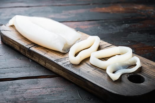 Raw squid meat on wooden cutting board on old wooden dark table, food photo.