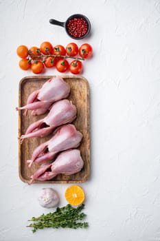 Whole quails meat with spices, herbs, vegetables, top view, on white textured background with copy space