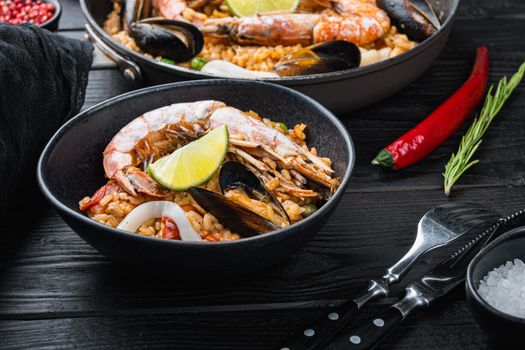 Homemade spanish seafood paella in frying pan and black bowl on black wooden background, food photo.