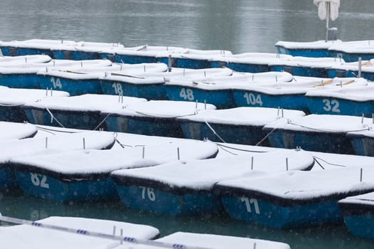Madrid, Spain - January 08, 2021: Boats covered with snow and moored in the Estanque Grande del Retiro, Madrid, in the middle of a snowy day, due to a wave of polar cold.