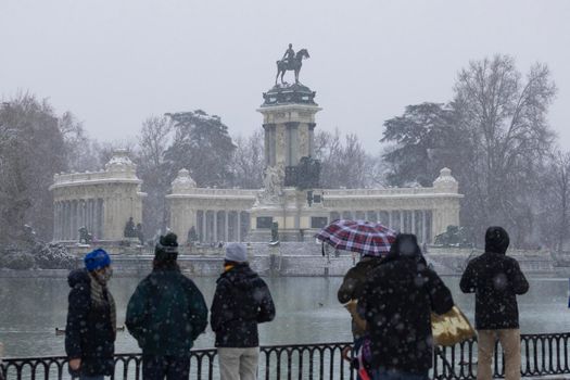 Madrid, Spain - January 08, 2021: People enjoying a walk through the Buen Retiro park in Madrid, in the middle of a snowy day, due to a wave of polar cold.