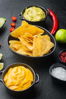 Nachos and guacamole and cheese sauces, on black background