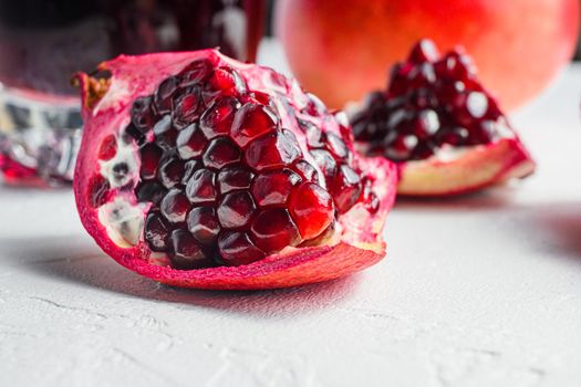 Pomegranate cut with seeds close up in front of garnet cut and juice in glass side view, on white background, selective focus.