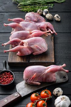 Whole quails meat with spices, herbs, vegetables, on black wooden background
