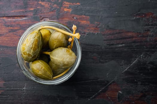 Capers, marinated in oil, on old wooden table, top view with copy space for text