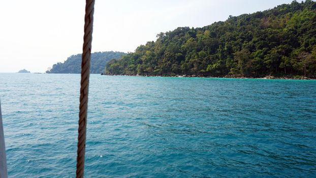 Travel by sea in Thailand by ship. View of the open ocean, green Islands and gray sky in smog. Green water with waves. Sailing between the Islands. Ship from different sides: stern, bow, rope, anchor.