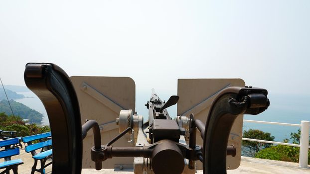 Observation deck with a military cannon. Machine gun on the shore. Protecting the island. Military weapons, army. History of the battle. A large caliber. Memory of the battle. Chang Island, Thailand.