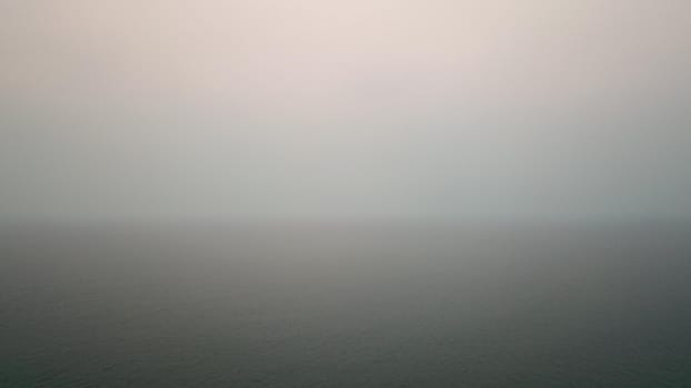 Due to a fire in Cambodia, heavy smoke obscures visibility in the sea. Nothing is visible, just a dark sea and a white fog. Flight to the sea, horizon. Shooting from a drone. Fearfully.