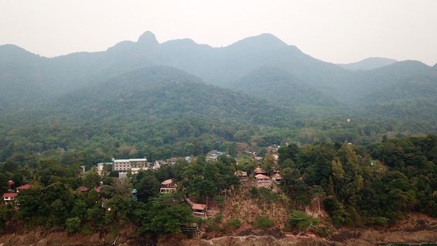 Green Chang island is covered in smoke from a fire in Cambodia. Green trees, palm trees and hills are covered with clouds of smog. Hotels stand on a cliff in front of the sea. Turquoise water.