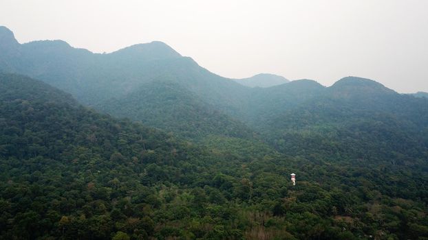 Green Chang island is covered in smoke from a fire in Cambodia. Green trees, palm trees and hills are covered with clouds of smog. Hotels stand on a cliff in front of the sea. Turquoise water.