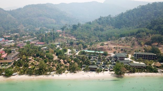 Green Chang island is covered in smoke from a fire in Cambodia. Green trees, palm trees and hills are covered with clouds of smog. Hotels stand on a cliff in front of the sea. Turquoise water.