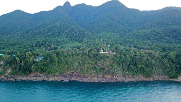 Green Chang island is covered in smoke from a fire in Cambodia. Green trees, palm trees and hills are covered with clouds of smog. Hotels stand on a cliff in front of the sea. Turquoise water.