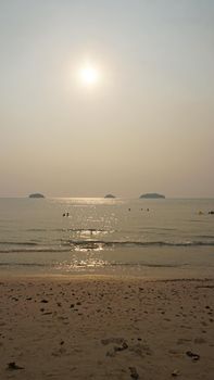 Smog obscures the sun's rays. People relax on the beach. Yellow rays of light. View of the islands, sand, sea and palm trees. Dirty air, smog. Chang Island, Thailand.