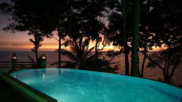 Incredible views of the pool and sunset. The bright colors of the setting sun and the orange sea. Turquoise water in the pool. Large palm leaves and trees as shadows. Lights are on. Relax. Koh Chang