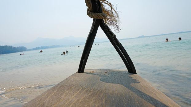 The beach of Koh Chang. Green leaves of trees and palm trees on the beach. Swings, garlands, and lanterns hang from the branches. Small waves from the sea. Green island, clean beach, people relax.