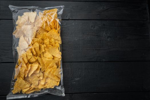 Corn traditional triangle nachos transparent pack, on black wooden background, top view or flat lay with copy space for text