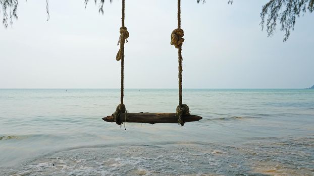 The beach of Koh Chang. Green leaves of trees and palm trees on the beach. Swings, garlands, and lanterns hang from the branches. Small waves from the sea. Green island, clean beach, people relax.