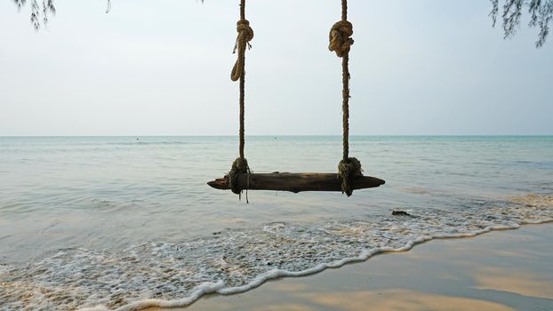The beach of Koh Chang. Green leaves of trees and palm trees on the beach. Swings, garlands, and lanterns hang from the branches. Small waves from the sea. Green island, clean beach, people relax.