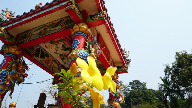 Chinese temple on Koh Chang island of Thailand. Bright colors of the temple, dragon and elephant sculptures. Flowers all around. The smoke from the sticks is coming. Hieroglyphs on the walls of bell.