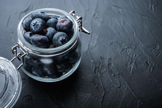 Ripe blueberry in glass jar with space for text, on black background.