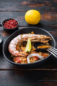 Sea food specialties paella in bowl on old dark wooden table, food photo.