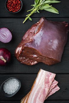 Raw liver with bacon and onion on black wooden background, flat lay.