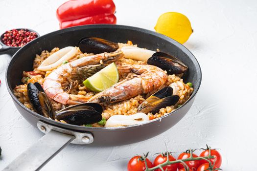 Seafood and chicken paella with rice, mussles, shrimps,chicken, tomatoes and wine in pan on white textured background, food photo.