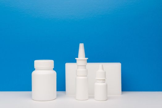 Still life with nose spay, eye drops and medication bottle on white table against blue background. Concept of healthcare and pharmacy