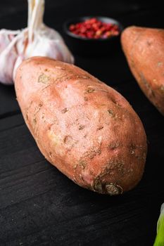 Sweet potato or batat with ingredients, on black wooden background.