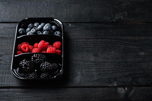 Fresh berries packed in tray, blueberries, raspberry and blackberry with space for text, on black wooden table