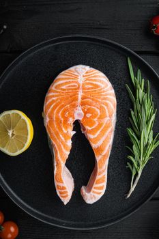 Salmon steak raw fish with herbs, on black wooden surface, top view.