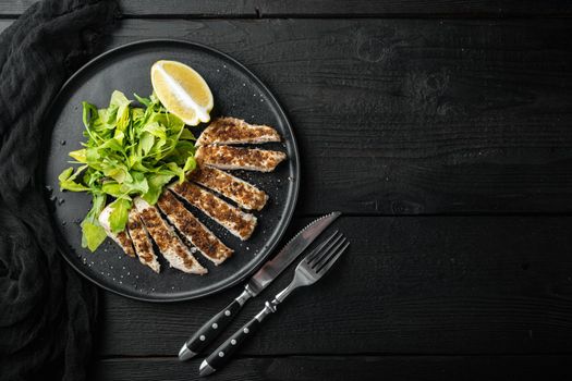 Crumbed, chicken breast fillet grilled, over black wooden table, flat lay with copy space